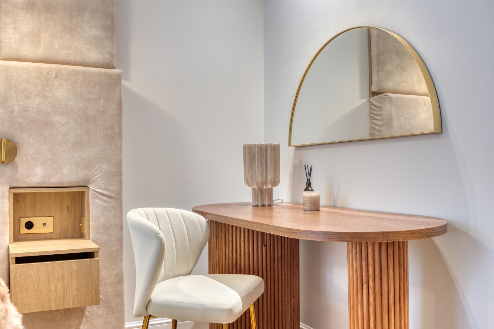 Détail d'une chambre rénovée à Paris : tête de lit capitonnée avec niche en chêne et prise intégrée, bureau en bois cannelé et miroir demi-lune
